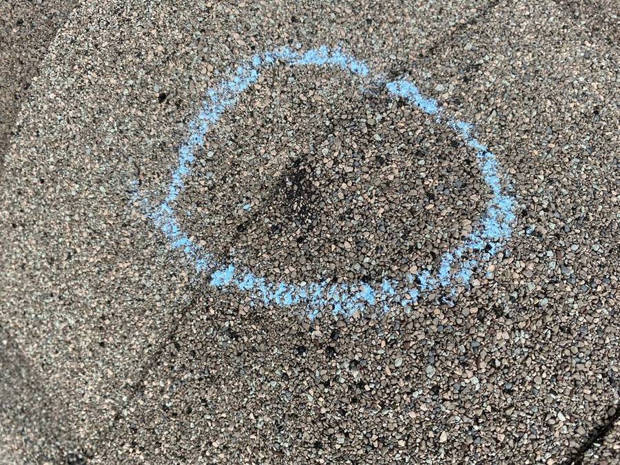 Close-up of hail damage on a shingle marked with blue chalk during inspection